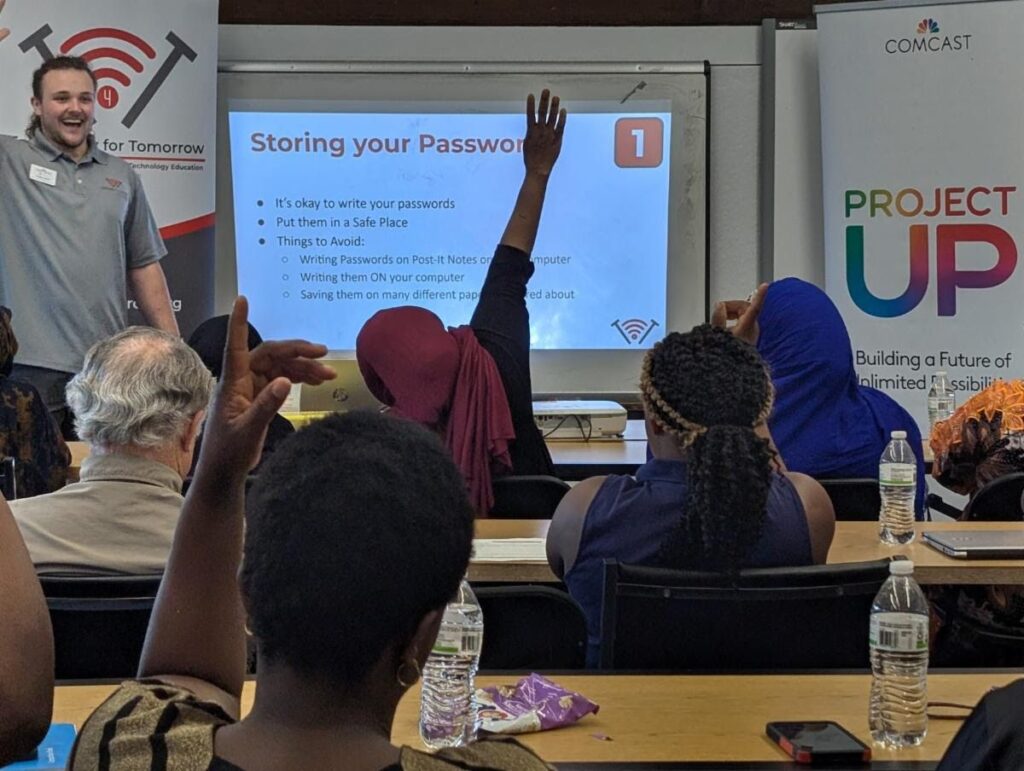 A class of New American students raising their hands with T4T instructor Wolde North