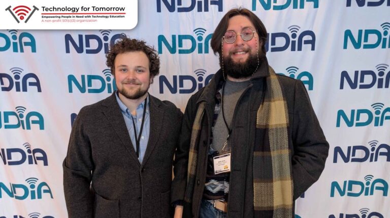 A photograph of Wolde North, a man with curly brown hair and a short beard, and Maliki LaForce, a tall man with straight hair and a full beard, standing in front of a banner for the National Digital Inclusion Alliance.